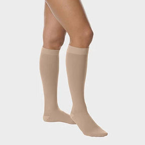 A model's legs wearing beige knee-high compression socks against a light gray background. - okotoks hc pharmacy