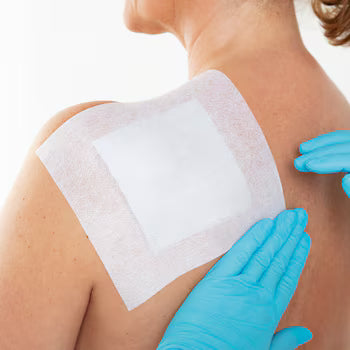 Person applying a white adhesive patch to their shoulder with blue gloves. - okotoks hc pharmacy