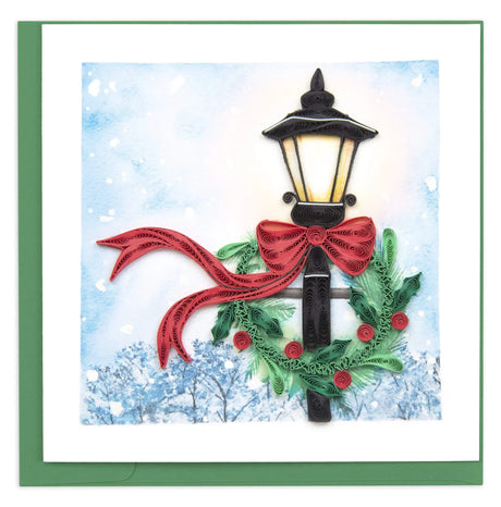 Decorative card with a Christmas-themed street lamp, red ribbon, and greenery against a snowy background. - okotoks hc pharmacy