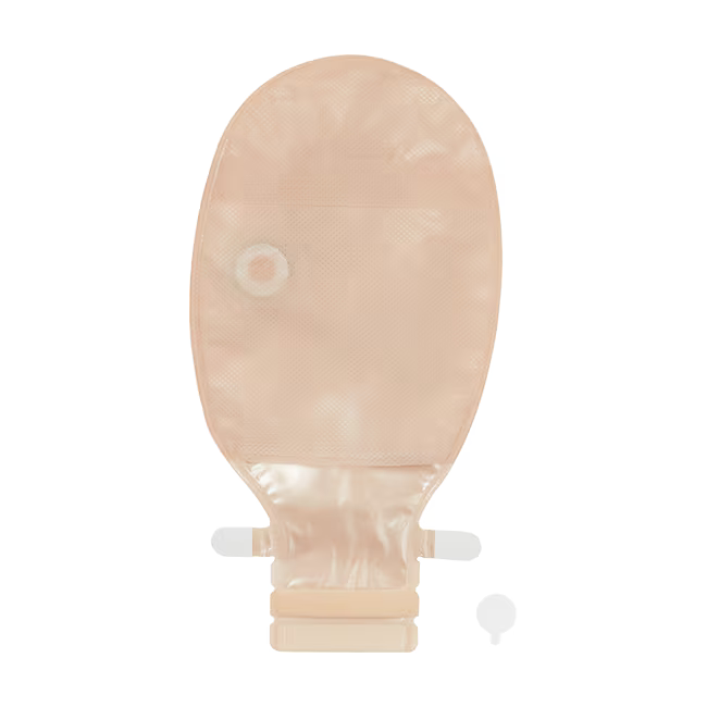 A beige skin-tone disposable abdominal ostomy bag with a central drain hole and a short connector tube, shown on a plain white background with a small matching accessory piece at the bottom right. - okotoks hc pharmacy