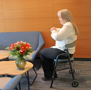 Person using a walker in a room with a gray couch and a table with flowers. - okotoks hc pharmacy