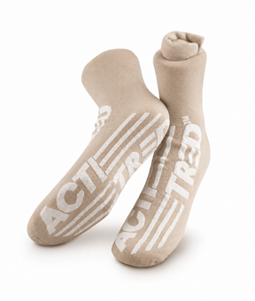 A pair of beige crew socks with bold white 'ACT! TREAD' text and stripe graphics on the soles, displayed against a clean white background. - okotoks hc pharmacy