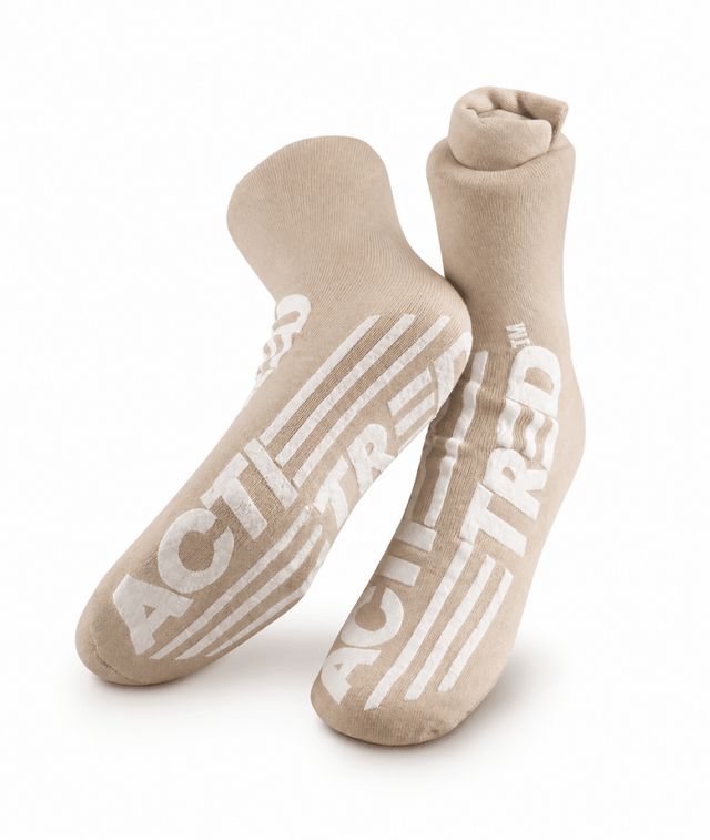 A pair of beige crew socks with bold white 'ACT! TREAD' text and stripe graphics on the soles, displayed against a clean white background. - okotoks hc pharmacy