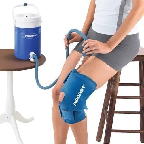 Person using a blue Cryo/Cuff compression device on their knee, with an Aircast cooler in the background. - okotoks hc pharmacy