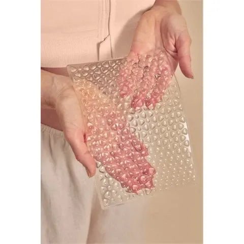 Hand holding a Amoena Large Lymph Flow Pressure Pad  against a beige background - okotoks hc pharmacy