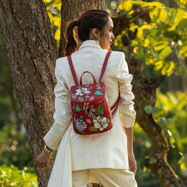 Woman in a white outfit with a red floral backpack standing next to a tree in a garden. - okotoks hc pharmacy