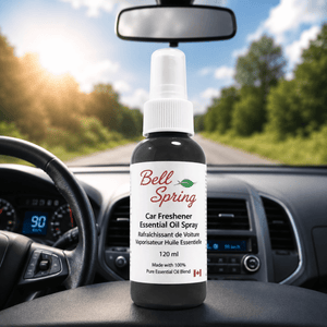 Bell Spring Car Freshener Essential Oil Spray bottle on a car dashboard with a blurred road and trees in the background. - okotoks hc pharmacy