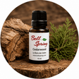 Bell Spring Cedarwood essential oil in a 15 ml amber glass bottle with a black cap and white label, styled on a rustic wood slice with a green cedar branch. - okotoks hc pharmacy