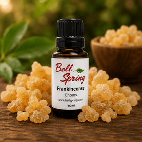 A small amber glass bottle of Bell Spring Frankincense with a black cap and white label, surrounded by loose yellow-orange frankincense buds on a wooden surface with a blurred green background. - okotoks hc pharmacy