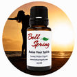 A 15 ml amber glass essential oil bottle with a black cap and a white label reading 'Bell Spring' and 'Raise Your Spirit', centered over a circular beach sunset background with a silhouetted person. - okotoks hc pharmacy