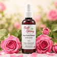 A bottle of Bell Spring Rose Flower Distillate centered on a marble surface, surrounded by fresh pink roses and petals with a soft, blurred garden background. - okotoks hc pharmacy