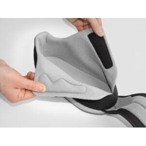 Gray knee brace with black straps held by a person on a light gray background - okotoks hc pharmacy