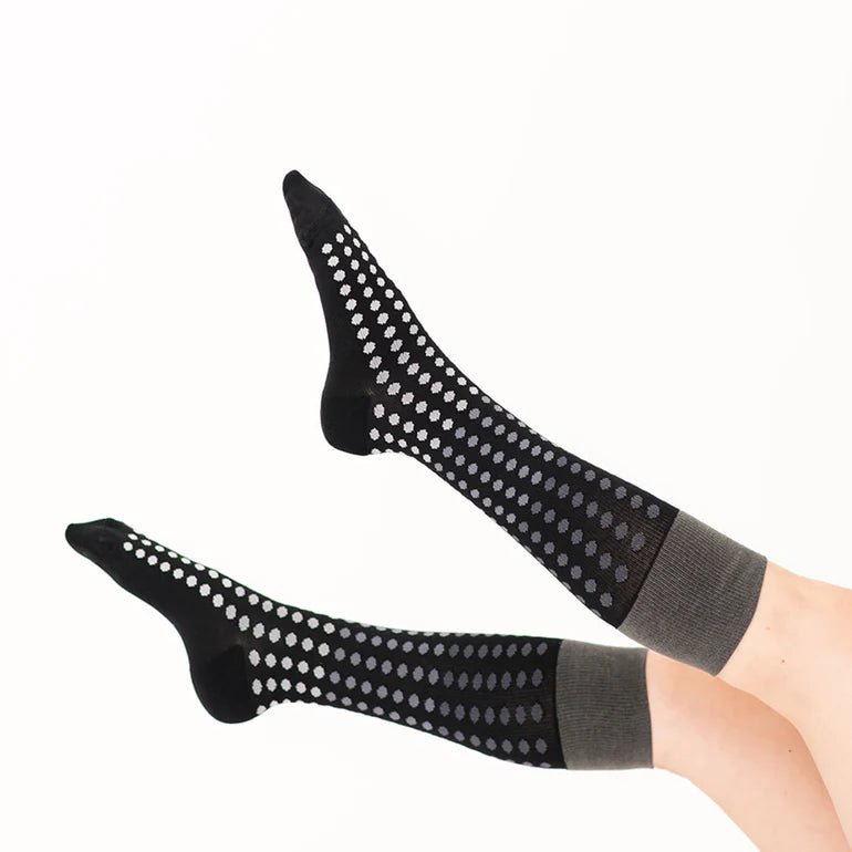 A pair of black knee-high socks with silver grip dots and gray ribbed cuffs, shown on a person's legs against a plain white background. - okotoks hc pharmacy