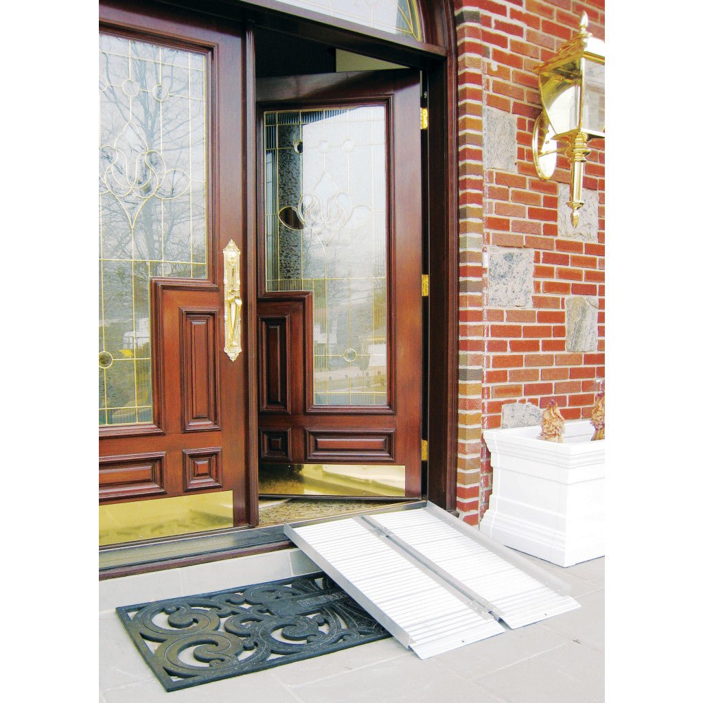 Wooden front door with glass panels and a white wheelchair ramp leading up to it, on a brick wall background. - okotoks hc pharmacy