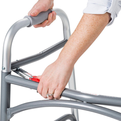Person using a silver walker with red brake handle on a white background - okotoks hc pharmacy