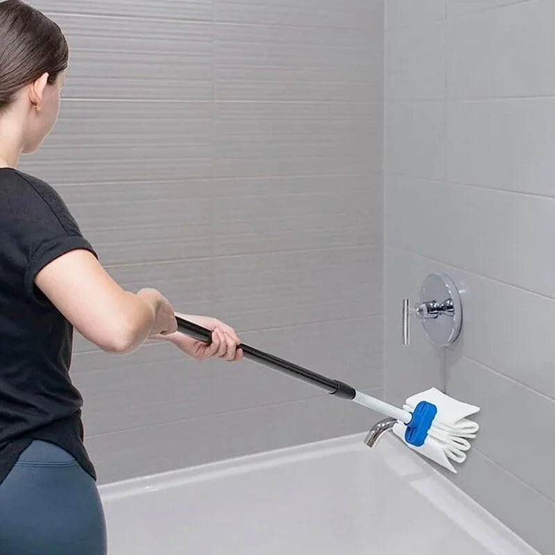 A woman in a black t-shirt and gray leggings uses a long-handled cleaning tool with white gloves and a blue scrubber attachment to clean a bathtub in a tiled shower area. - okotoks hc pharmacy