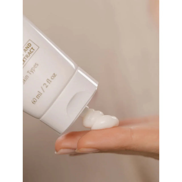 Hand holding a tube of skincare product with a small amount of cream on a neutral background - okotoks hc pharmacy