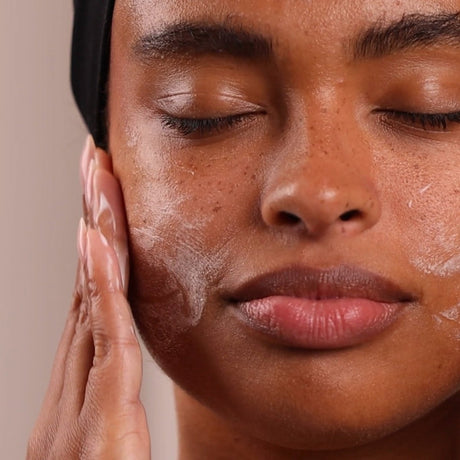 Close-up of a person applying skincare product to their face with a neutral background - okotoks hc pharmacy