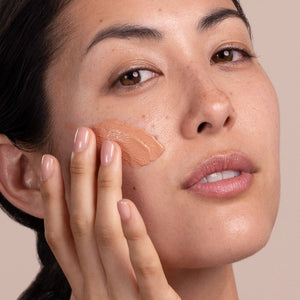 Woman applying a cosmetic product to her face with a neutral background - okotoks hc pharmacy