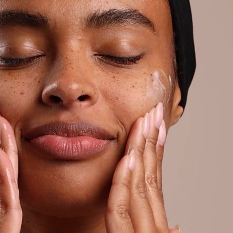 Woman applying cream to her face with a neutral background - okotoks hc pharmacy