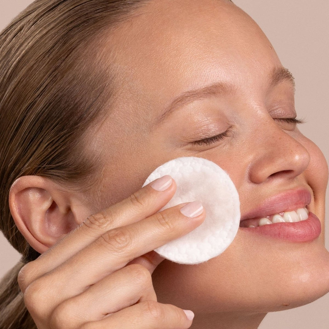 Woman applying a white cotton pad to her face against a neutral background - okotoks hc pharmacy