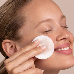 Woman applying a white cotton pad to her face against a neutral background - okotoks hc pharmacy