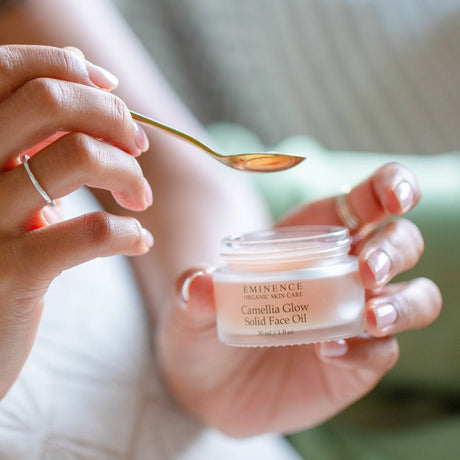 Person holding a small jar of Eminence Camellia Glow Solid Face Oil with a spoon. - okotoks hc pharmacy