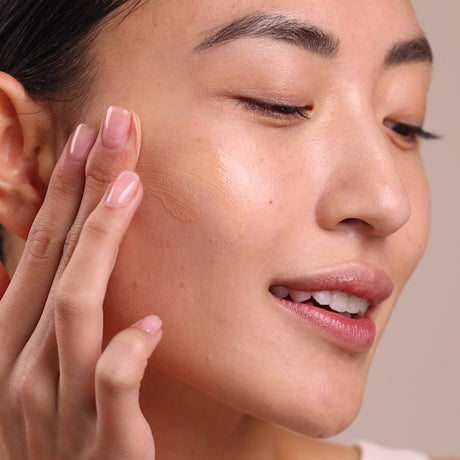 Woman applying a cosmetic product to her face with a neutral background - okotoks hc pharmacy