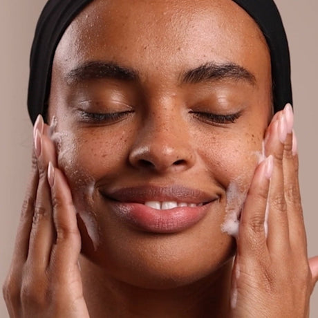 Woman applying a skincare product to her face with a neutral background - okotoks hc pharmacy