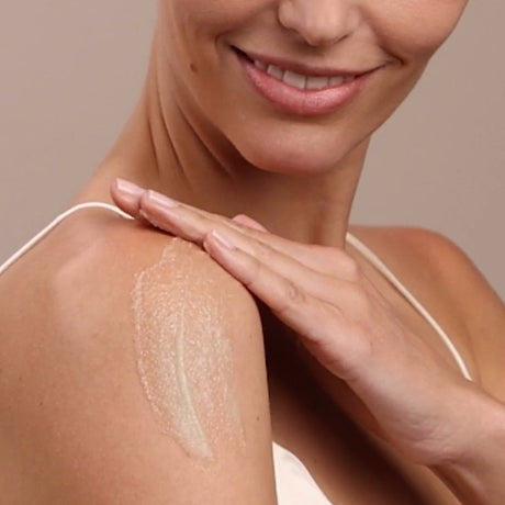 Woman applying cream to her shoulder on a beige background - okotoks hc pharmacy