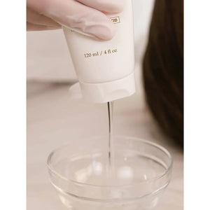 Hand holding a white bottle with a pump, dispensing liquid into a clear glass container on a light background. - okotoks hc pharmacy