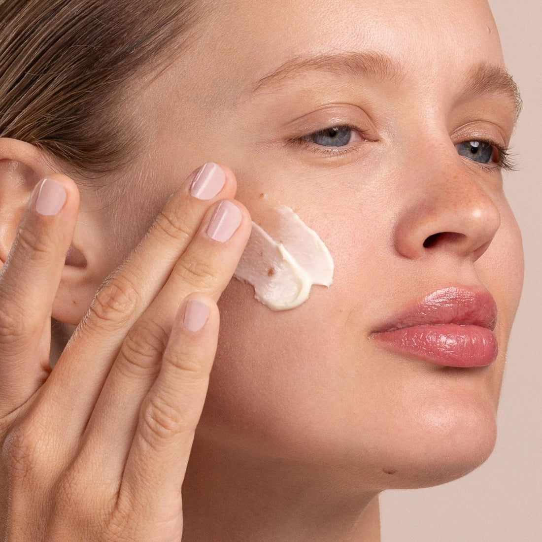 Woman applying cream to her face with a neutral background - okotoks hc pharmacy