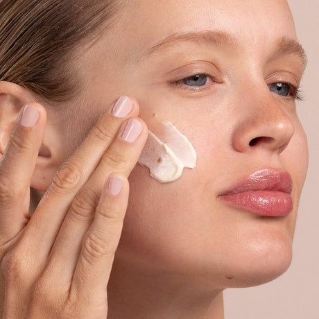 Woman applying cream to her face with a neutral background - okotoks hc pharmacy