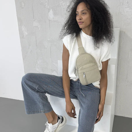 Woman sitting on a white chair wearing a white top, blue jeans, and a beige crossbody bag. - okotoks hc pharmacy