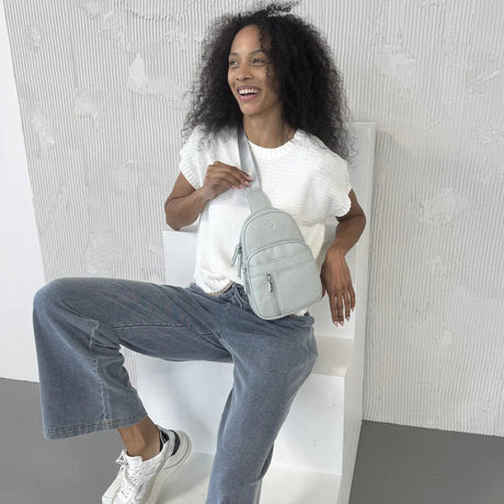 Woman sitting on a white chair holding a gray backpack against a light gray textured wall. - okotoks hc pharmacy