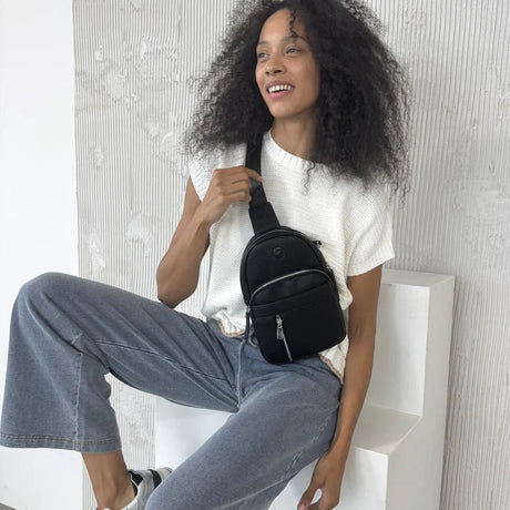 Woman sitting on a white bench holding a black bag against a light gray wall. - okotoks hc pharmacy