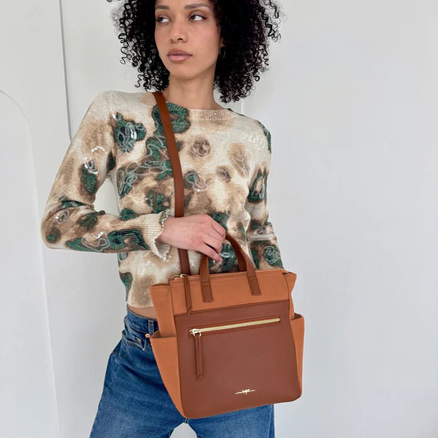 Woman holding a brown handbag against a plain background - okotoks hc pharmacy