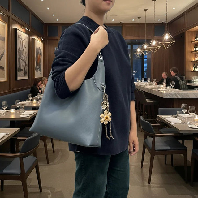 Person holding a blue handbag with a floral charm in a restaurant setting - okotoks hc pharmacy