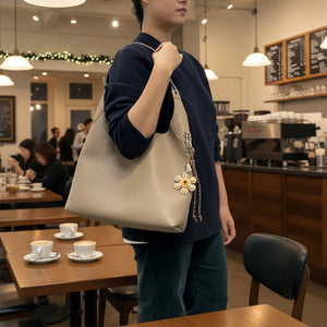 Person holding a beige handbag with a decorative flower charm in a coffee shop. - okotoks hc pharmacy