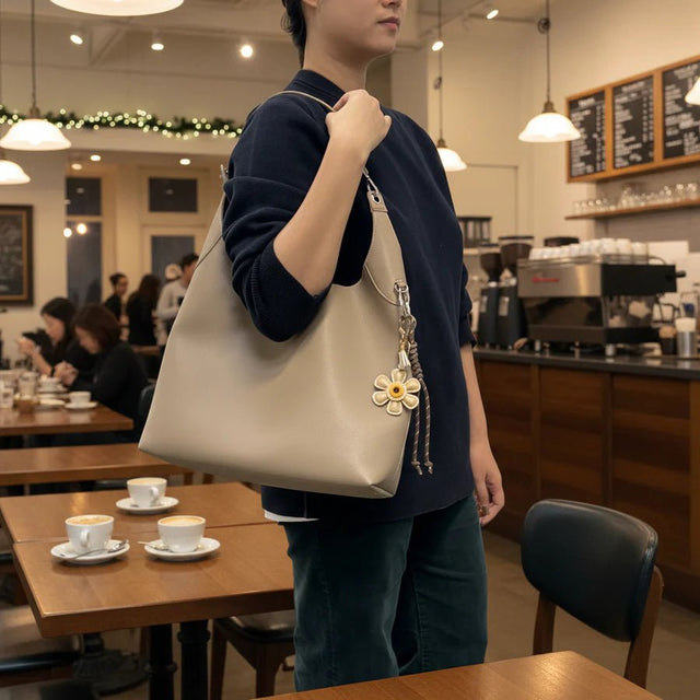 Person holding a beige handbag with a decorative flower charm in a coffee shop. - okotoks hc pharmacy
