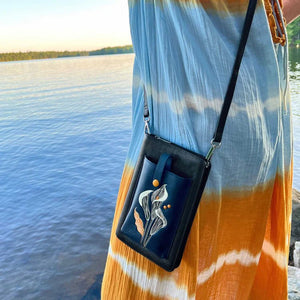 Black handbag with floral design held by a person wearing a tie-dye shirt by a lake. - okotoks hc pharmacy