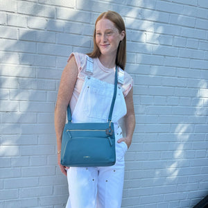 Woman holding a blue handbag against a light blue brick wall - okotoks hc pharmacy