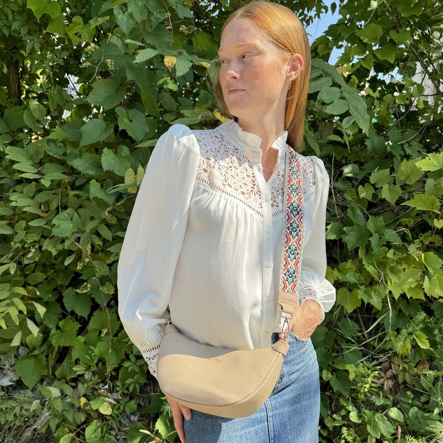 Woman wearing a white blouse with embroidery and blue jeans standing in front of green foliage. - okotoks hc pharmacy