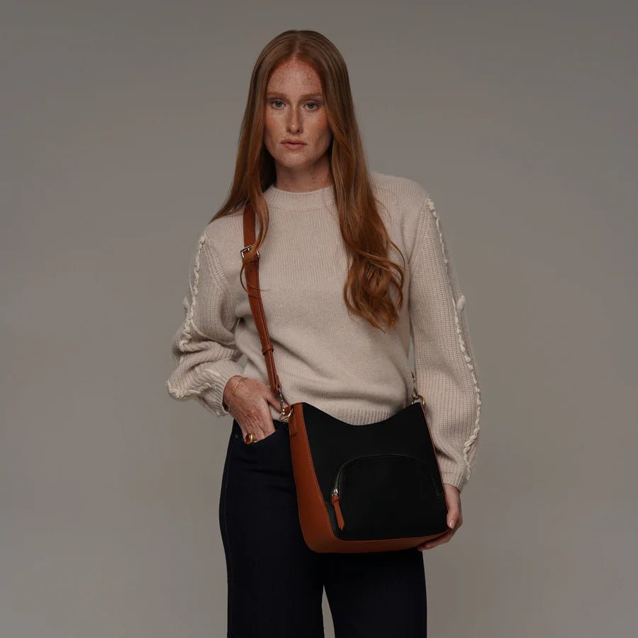 Woman holding a black handbag with a brown strap against a plain background - okotoks hc pharmacy