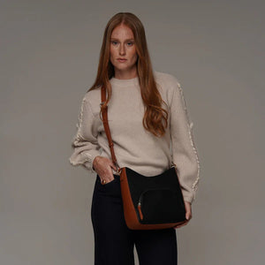 Woman holding a black handbag with a brown strap against a plain background - okotoks hc pharmacy