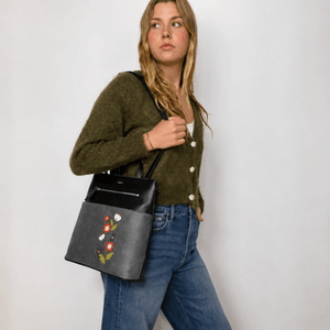 Woman holding a black handbag with floral embroidery against a plain background - okotoks hc pharmacy