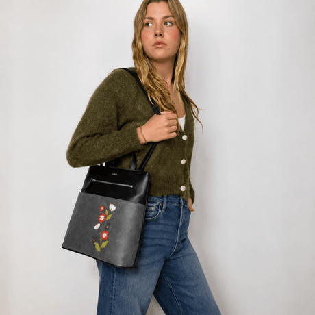 Woman holding a black handbag with floral embroidery against a plain background - okotoks hc pharmacy