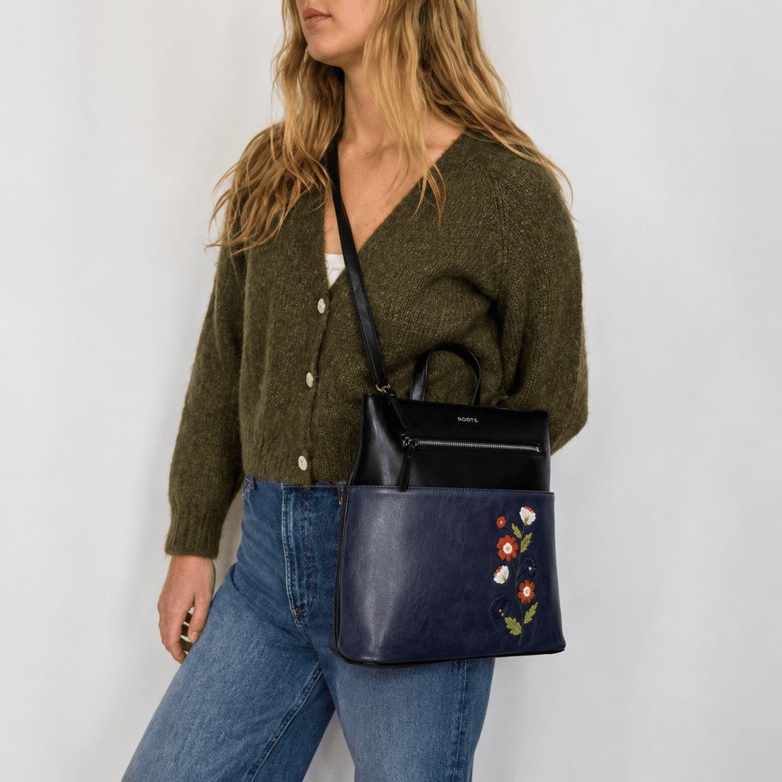 Woman wearing a green cardigan and blue jeans, holding a navy handbag with floral embroidery. - okotoks hc pharmacy