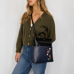 Woman wearing a green cardigan and blue jeans, holding a navy handbag with floral embroidery. - okotoks hc pharmacy