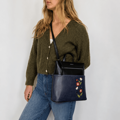 Woman wearing a green cardigan and blue jeans, holding a navy handbag with floral embroidery. - okotoks hc pharmacy